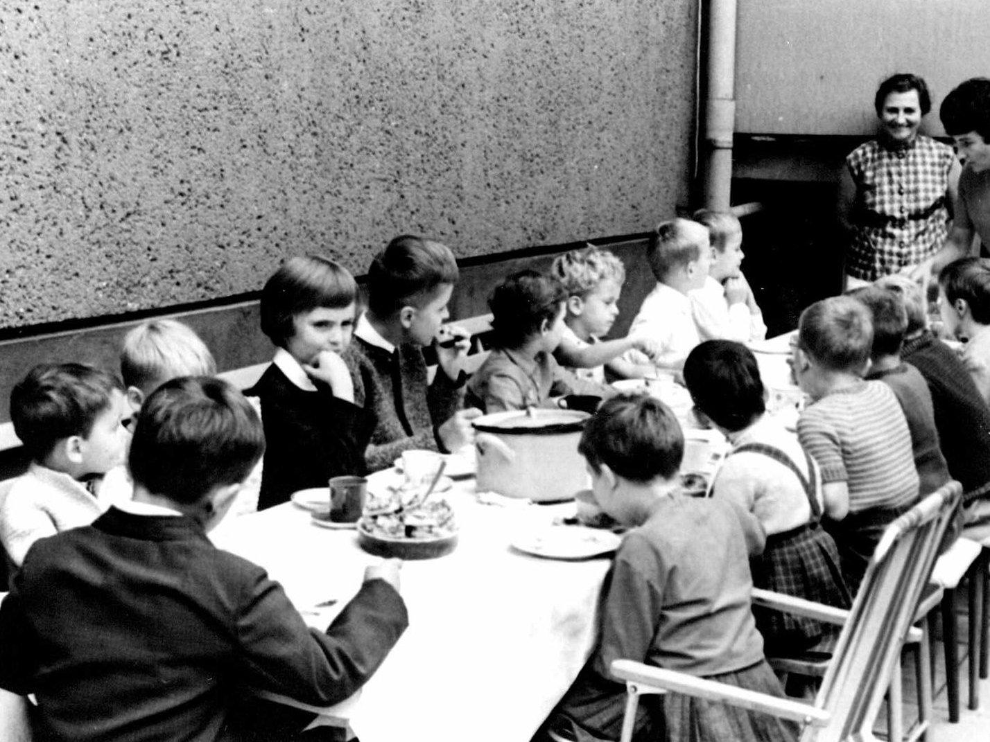 Kinder und Erzieher sitzen um einen Tisch beim Mittagessen